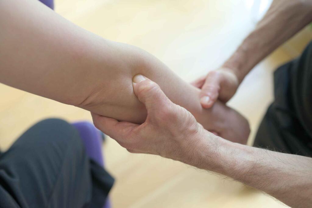 Close up therapist applying acupressure to client's flexor arm muscle.