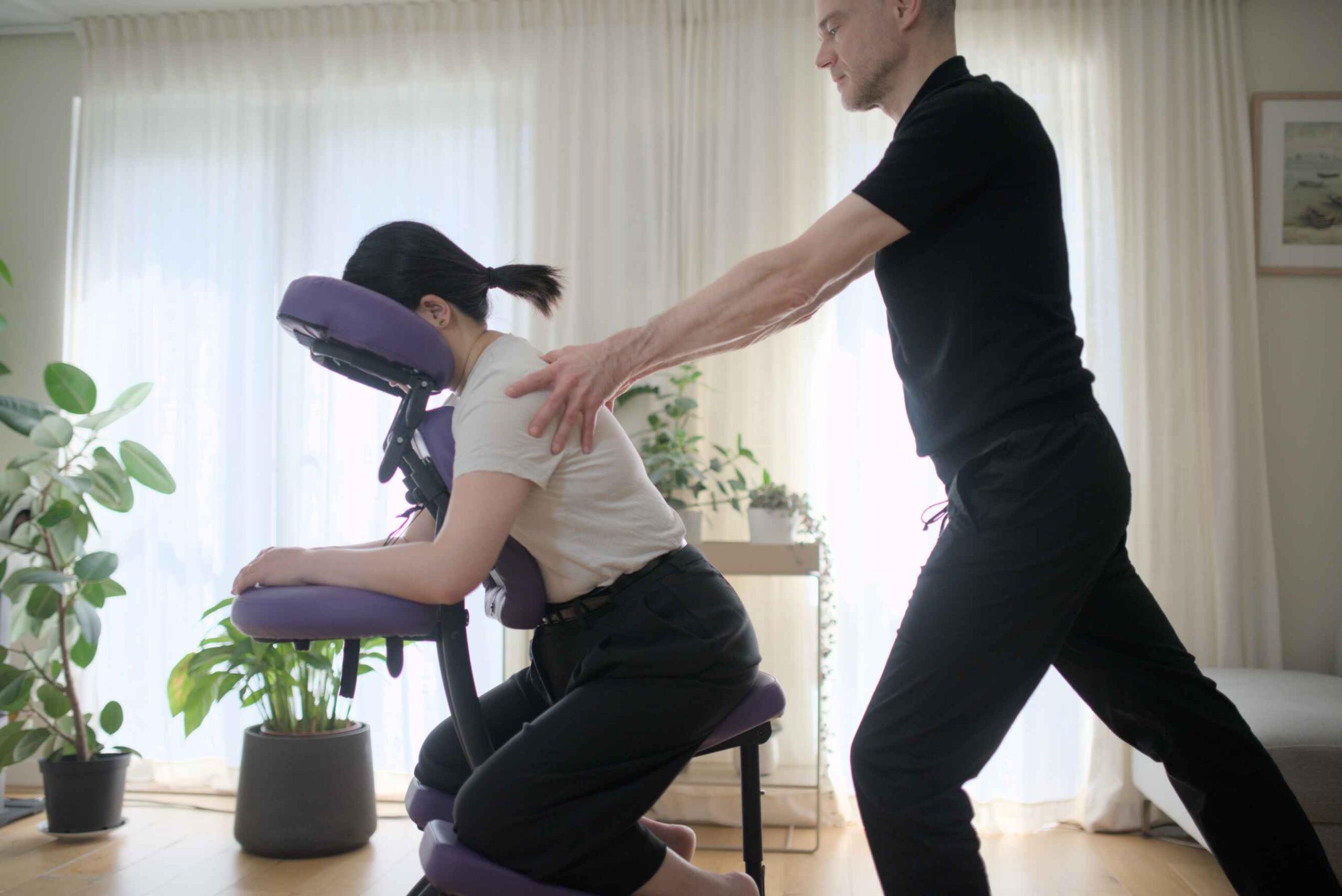 Therapist applying friction to rhomboid muscles, client in massage chair.
